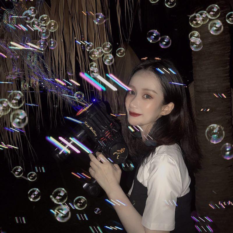 Woman in a black and white streetwear dress using a bubble gun at night, surrounded by bubbles.