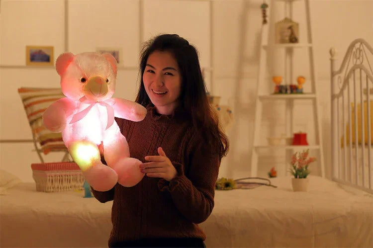 Woman in a brown knit sweater holding a glowing plush teddy bear in a cozy bedroom
