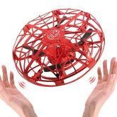 Red hand-operated flying drone toy with open lattice design hovering above hands