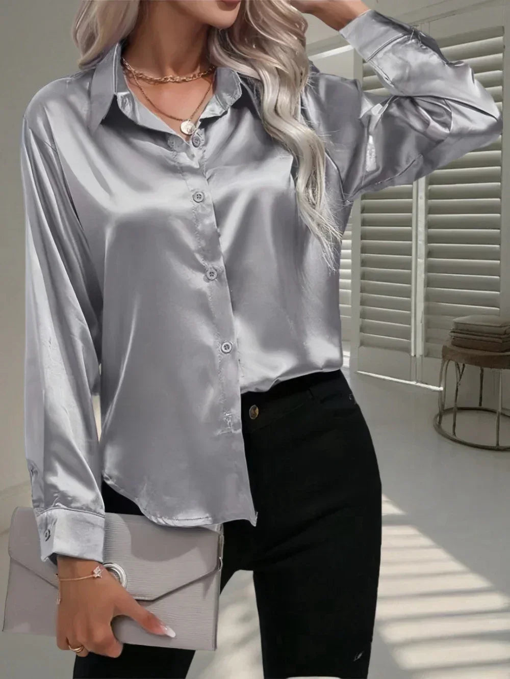Woman wearing a silver satin long sleeve button-up shirt with relaxed fit, paired with black pants