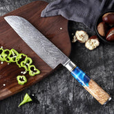 Patterned steel chef knife with blue resin and wood handle on cutting board with sliced peppers
