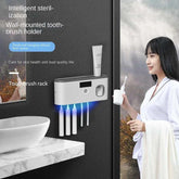 Woman in white robe holding towel near modern wall-mounted sterilizing toothbrush holder in bathroom.
