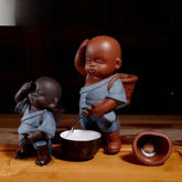 Two ceramic figurines in blue textured robes, loose fit, with baskets and water features