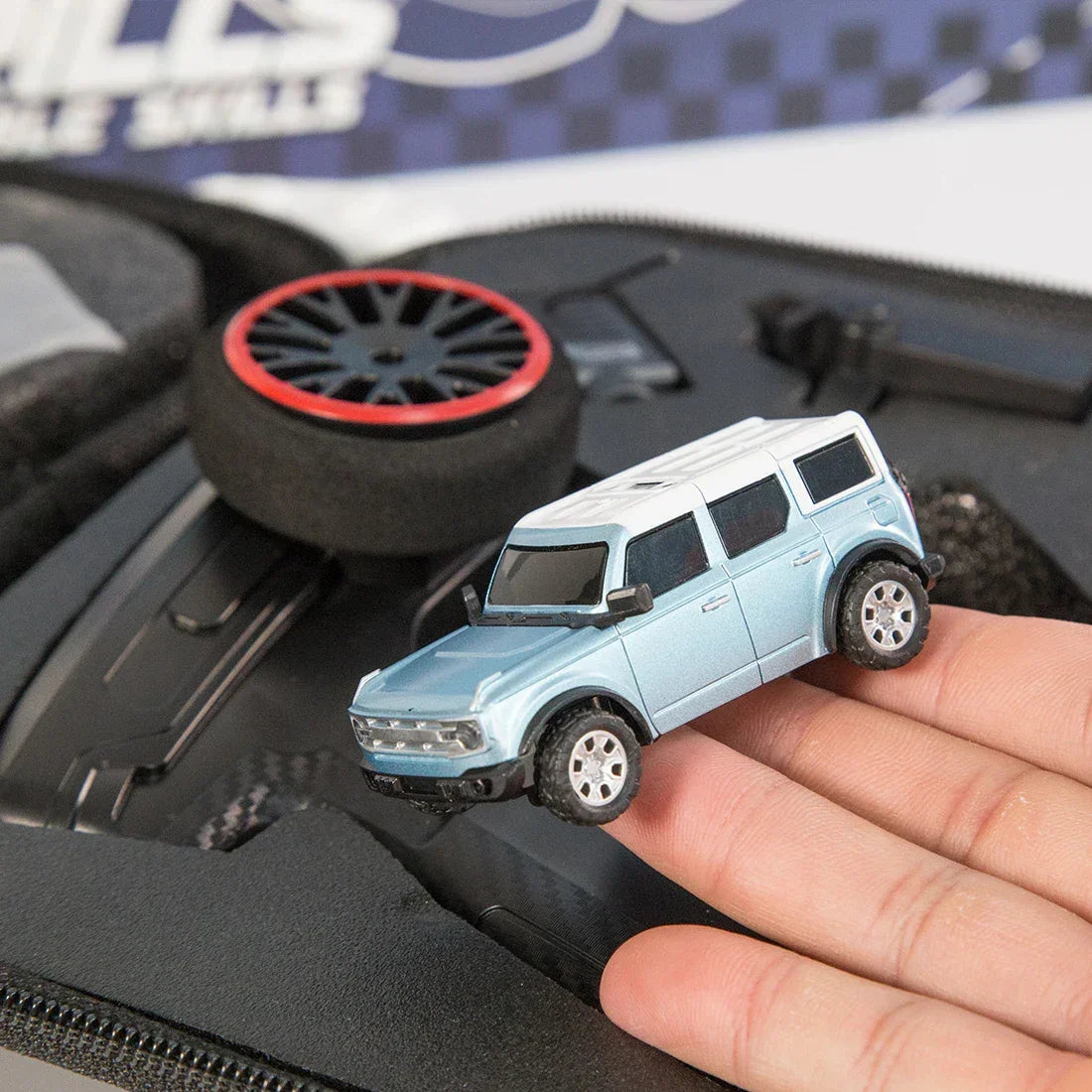 Hand holding a light blue and white miniature SUV toy car with black wheels, close-up.