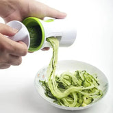 Handheld vegetable spiralizer making zucchini noodles over a bowl, white and green color