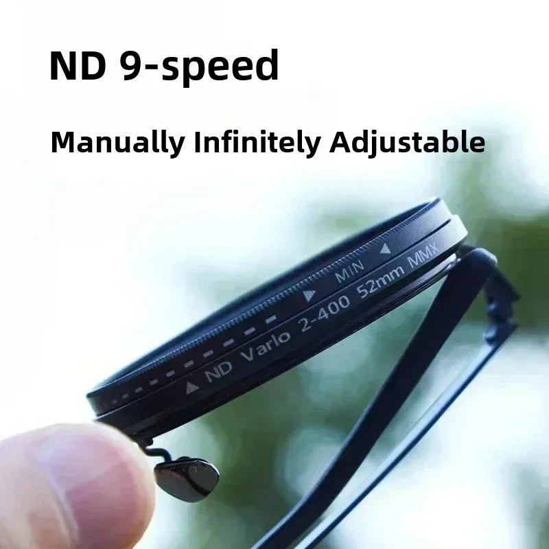 Hand holding slim black adjustable ND camera lens filter, marked 52mm, outdoors.