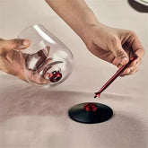 Hands assembling a modern glass cup with red metallic stem and black circular base on a beige surface.