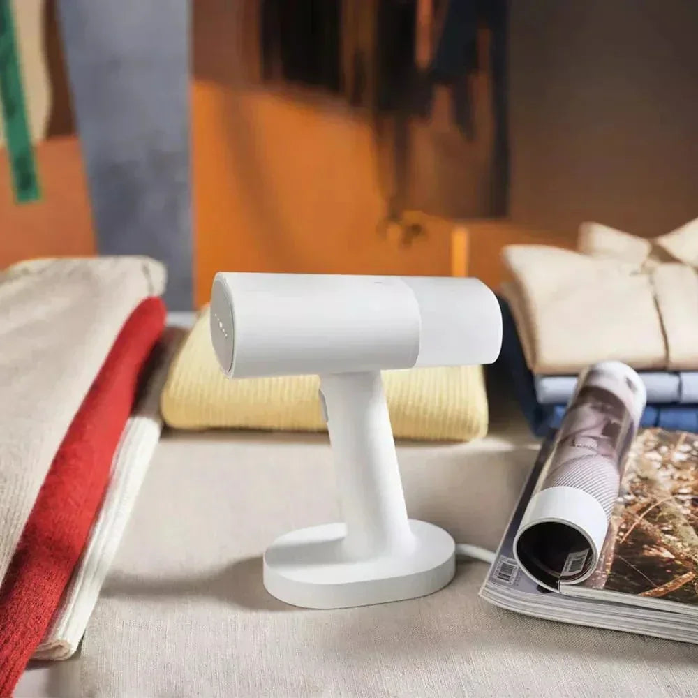 Folded knit sweaters in red, beige, and yellow, with a handheld garment steamer on a table