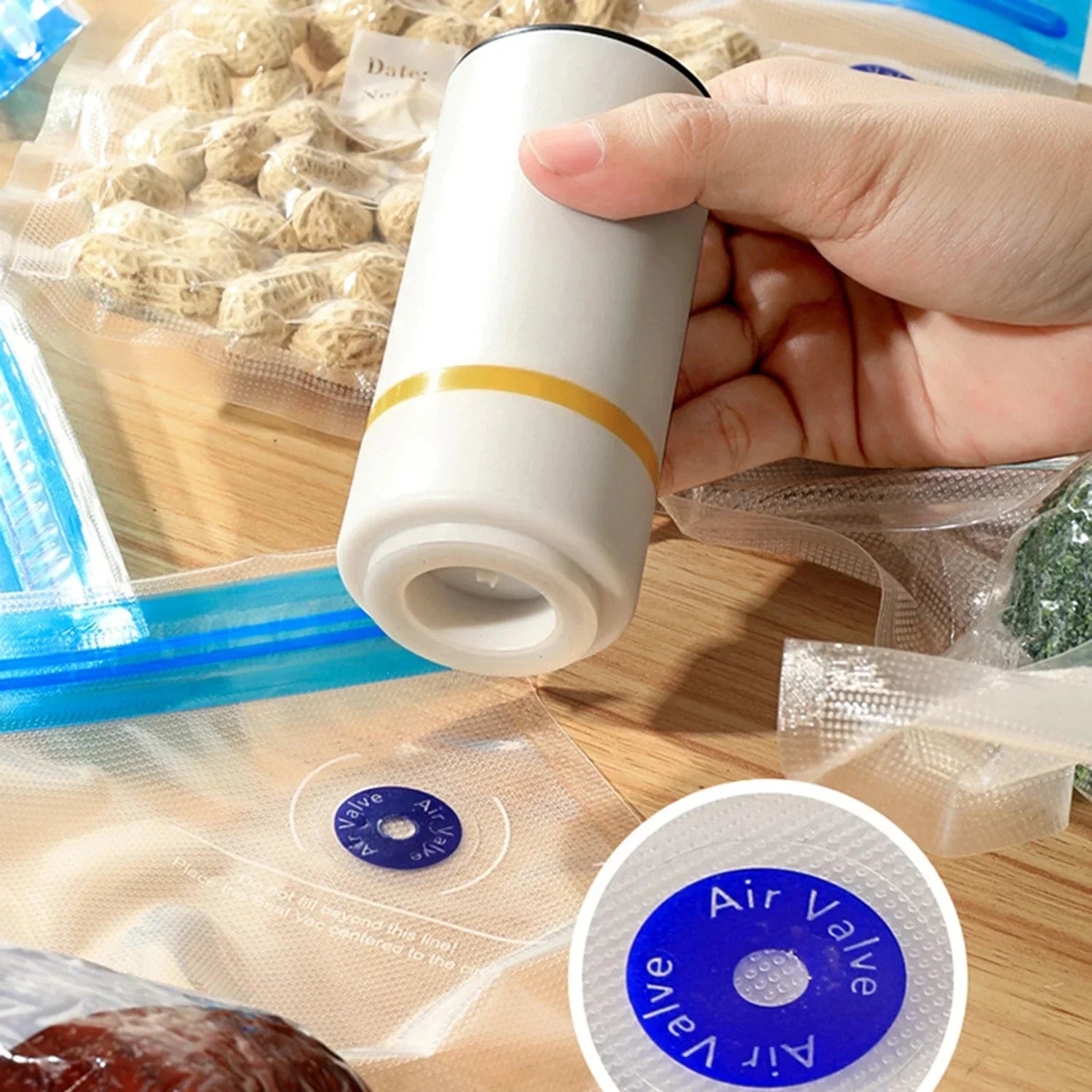 Hand holding portable vacuum sealer over clear vacuum bags for food storage on wood surface
