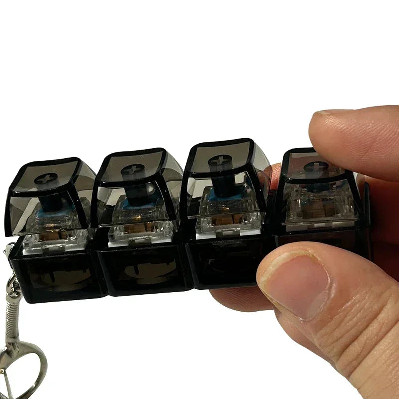 Hand holding a set of four black mechanical keyboard keycaps with transparent switches, compact design.