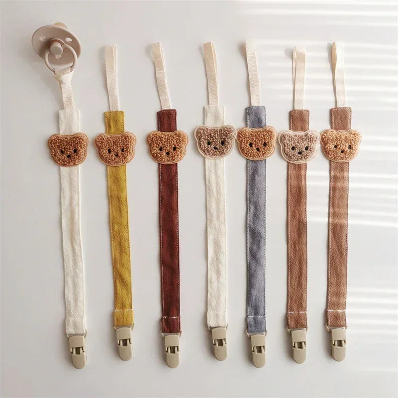 Cute bear-shaped pacifier clips in assorted soft fabric colors, neutral baby accessory.