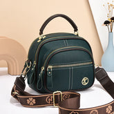 Dark green faux leather crossbody bag with gold zippers, top handle, and wide brown strap