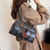 Woman in tan trench coat carrying a black leather satchel with buckle details and keychain accessories