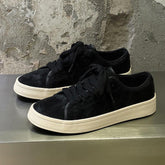 Black suede low-top sneakers with thick white soles and black laces, casual streetwear style.