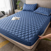 Quilted blue fitted mattress cover and matching pillows in a modern bedroom