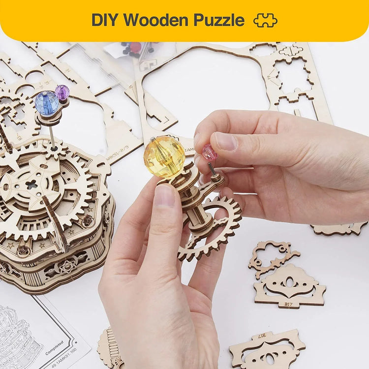 Hands assembling a DIY wooden gear puzzle with colorful crystal pieces on a white table.