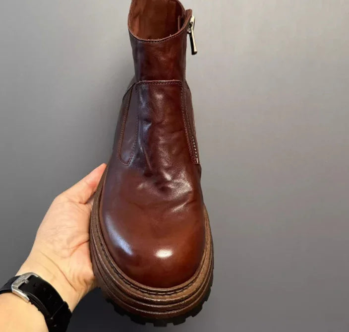 Hand holding a brown leather ankle boot with chunky sole and side zipper, streetwear style