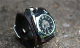Black leather wide cuff watch with silver accents and a skeleton dial on a textured surface