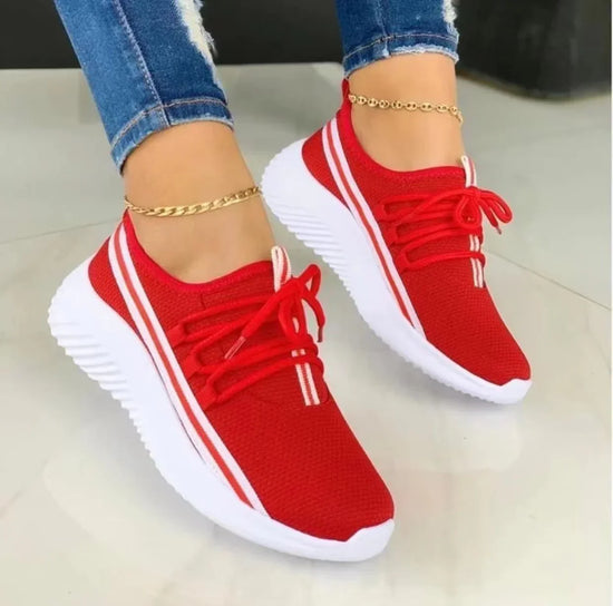 Red mesh sneakers with white soles and striped accents, sporty fit, paired with jeans.