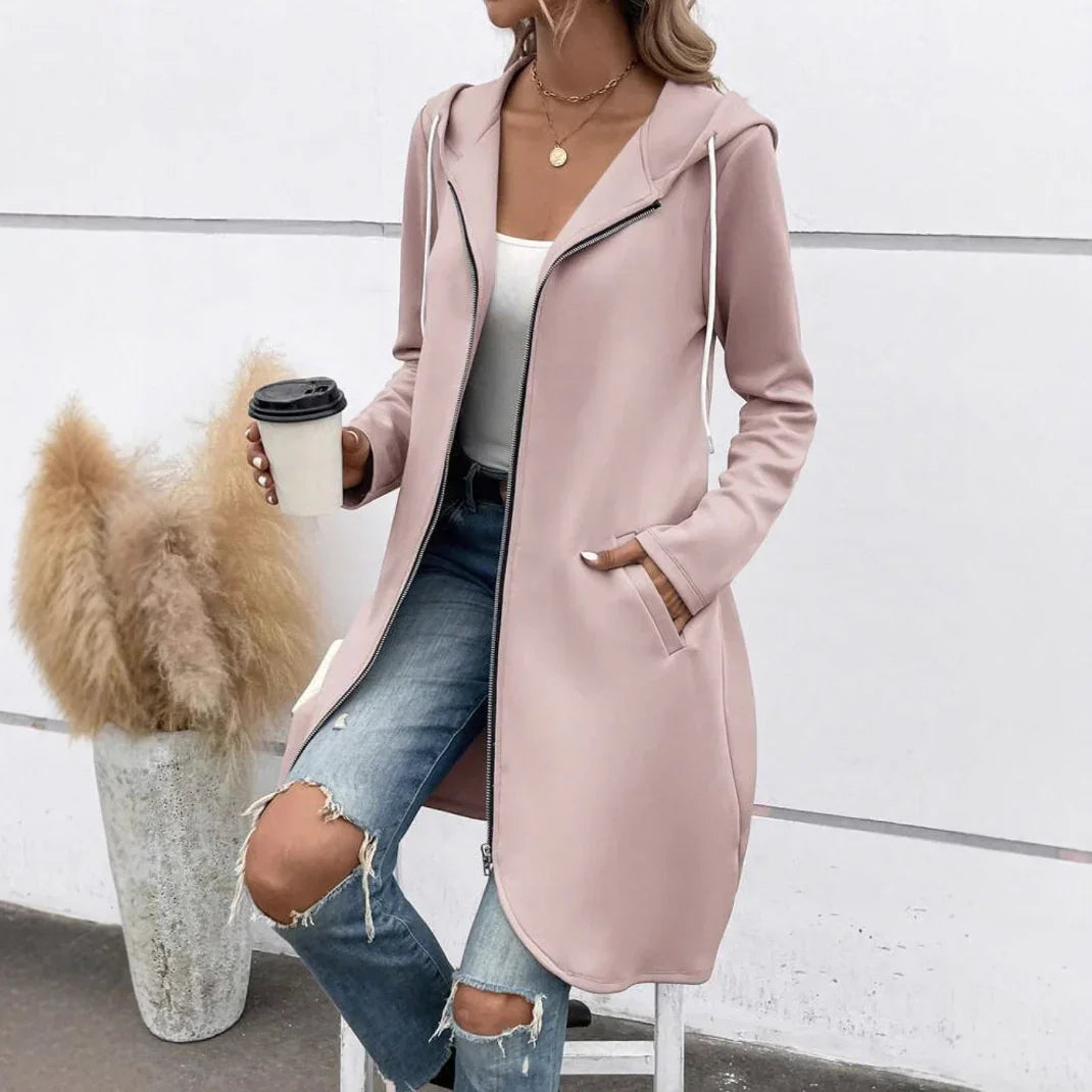 Woman wearing a light pink zip-up hooded coat, white tank top, and ripped blue jeans.