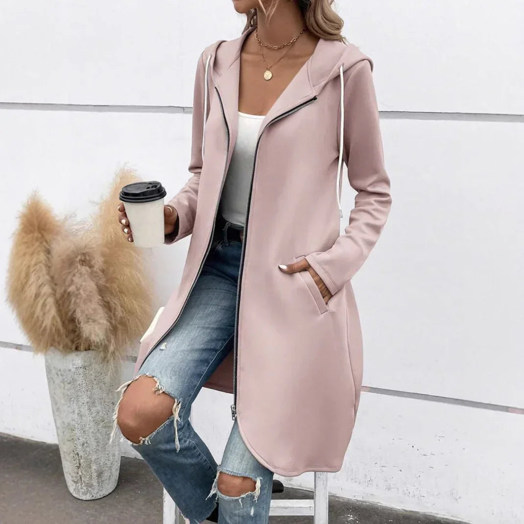 Woman wearing a light pink zip-up hooded coat, white tank top, and ripped blue jeans.