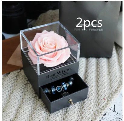 Gift box with a pink artificial rose and black drawer displaying blue beaded bracelets