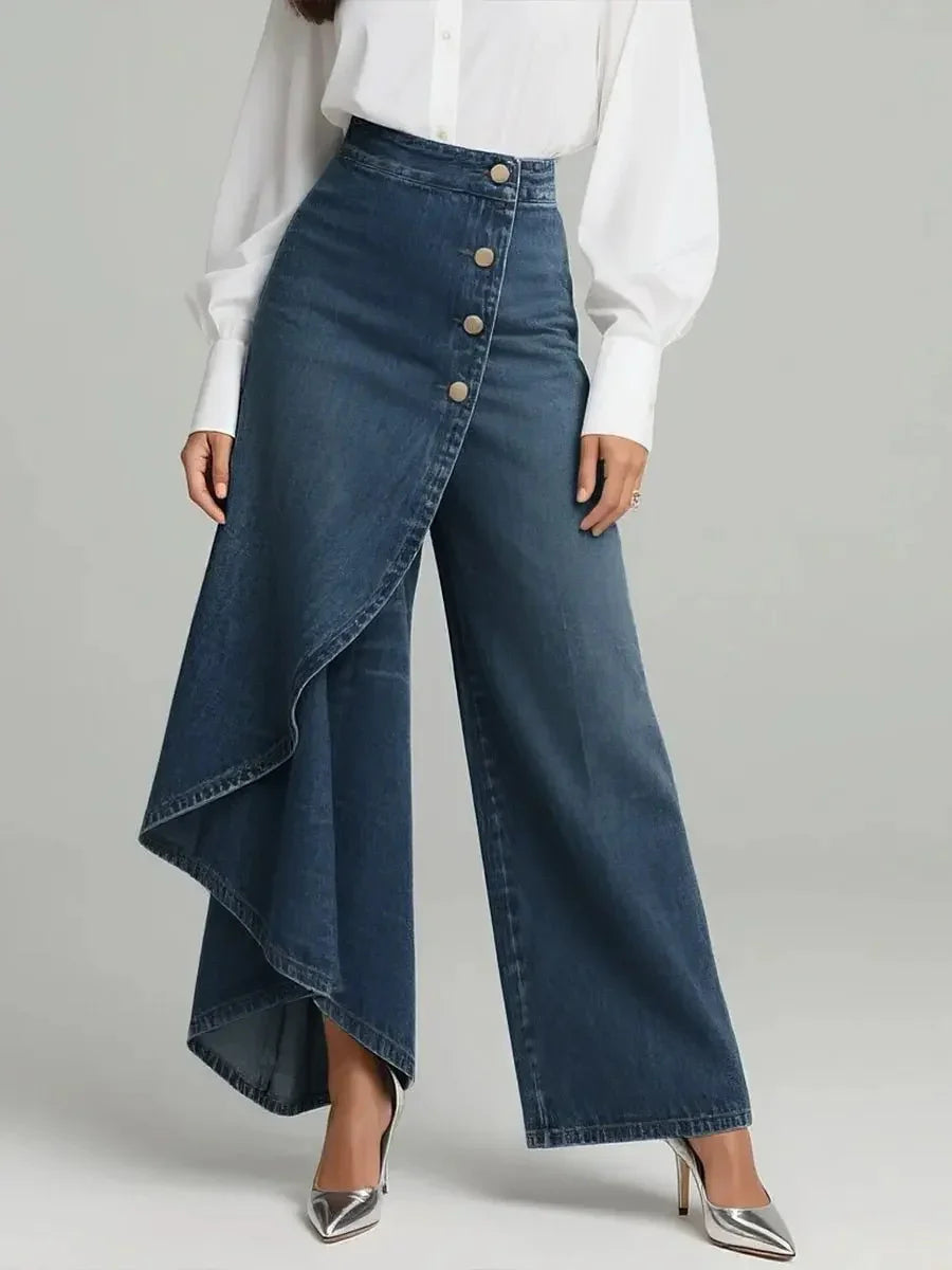 Asymmetrical high-waisted denim pants with wide legs and button details, paired with a white blouse