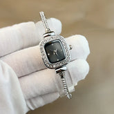 Elegant silver wristwatch with slim crystal-studded band, square black dial, and diamond accents.