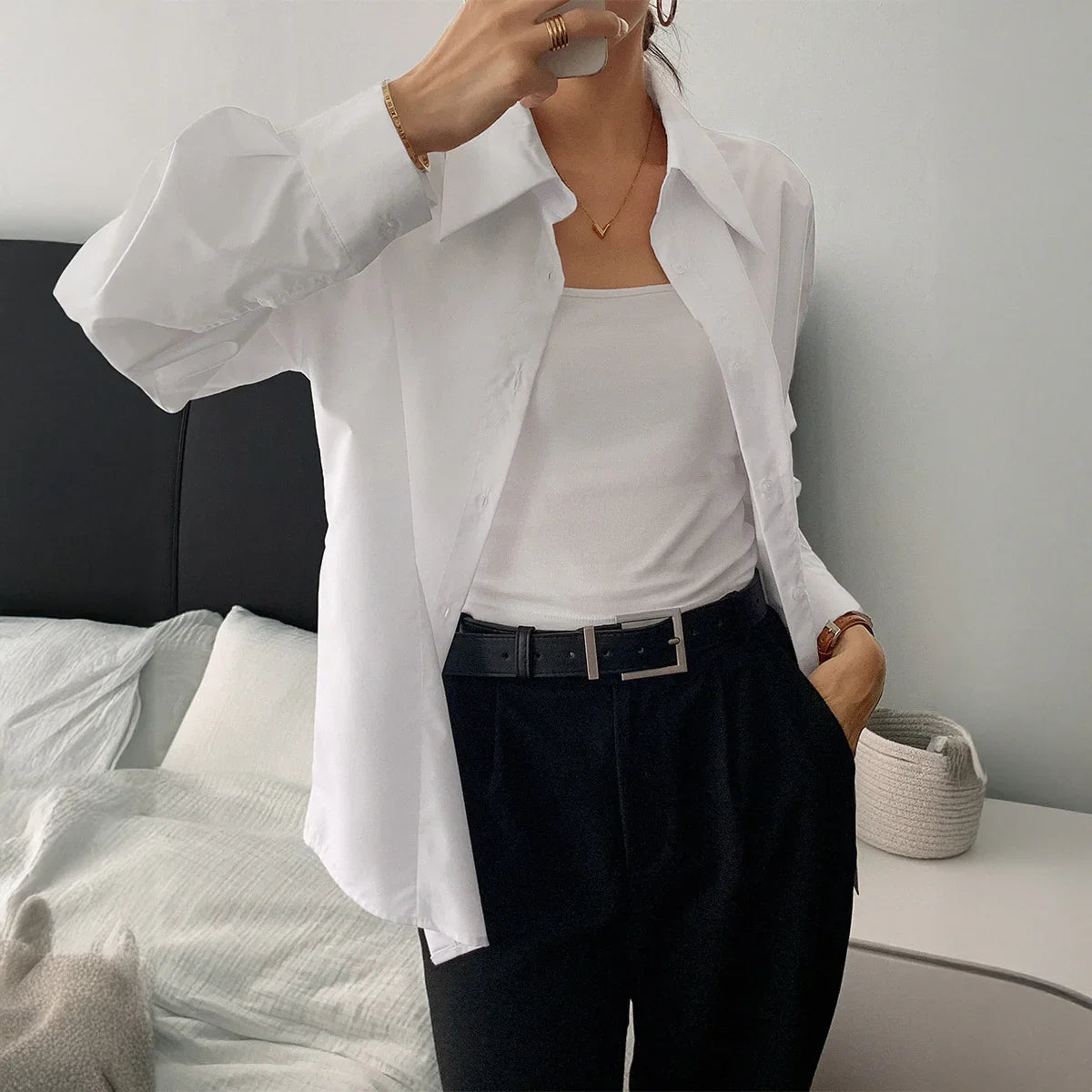 Woman in relaxed fit white cotton button-up shirt, white tank top, and black trousers