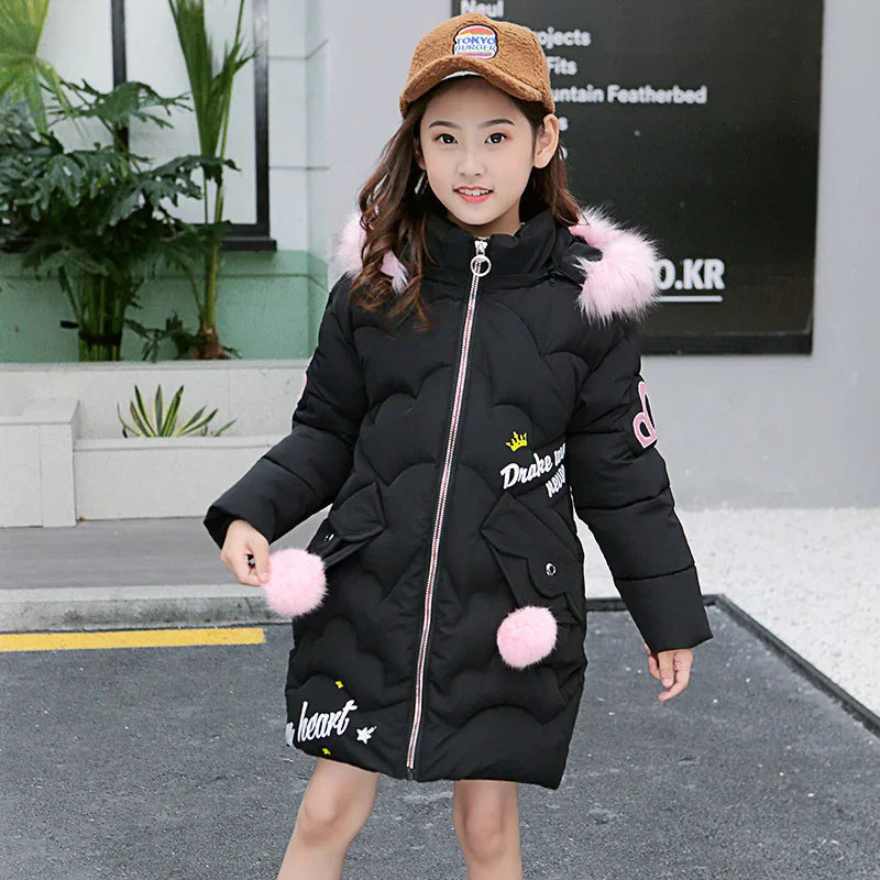 Girl in a long black puffer coat with pink faux fur trim and pom poms, casual street style