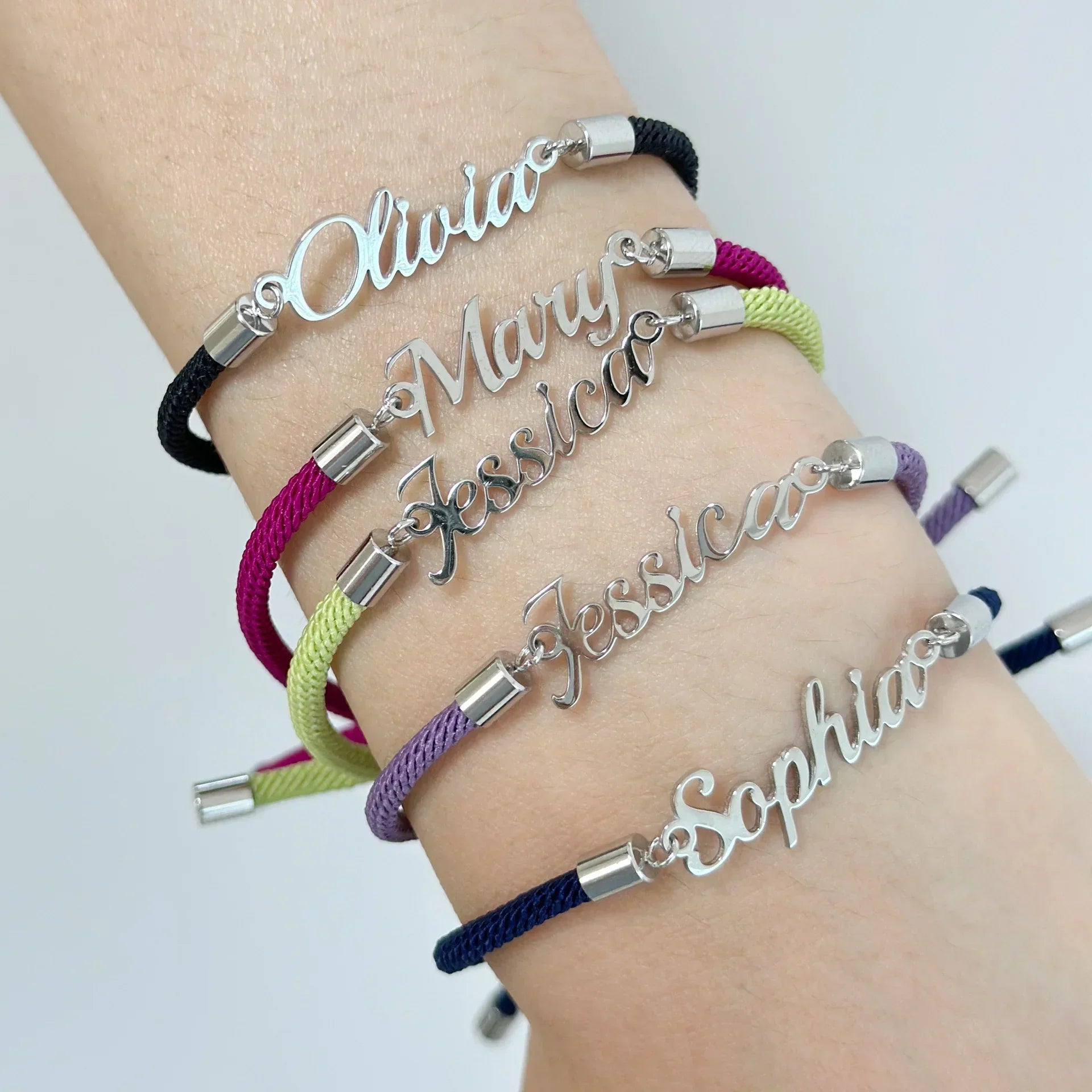 Stacked personalized nameplate bracelets with colored cords, silver tone, adjustable fit