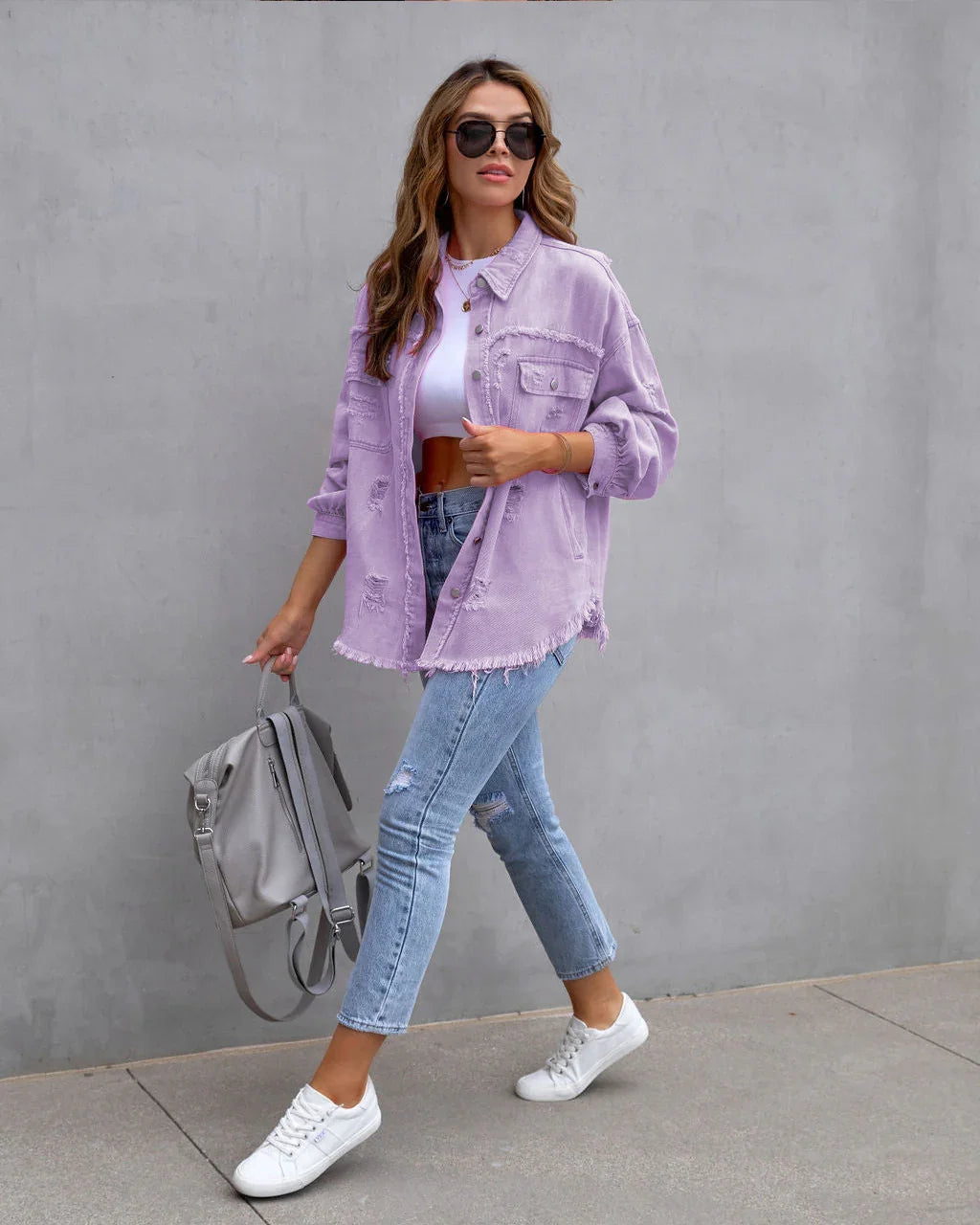 Woman in oversized lavender denim jacket, white crop top, ripped skinny jeans, and white sneakers