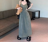 Woman wearing a long, sleeveless olive green denim dress with a fitted waist and relaxed fit.