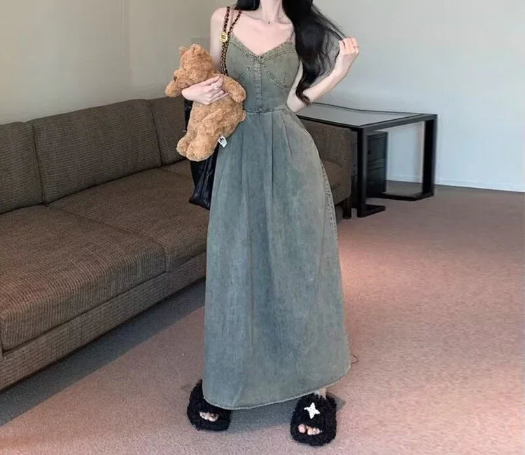 Woman wearing a long, sleeveless olive green denim dress with a fitted waist and relaxed fit.