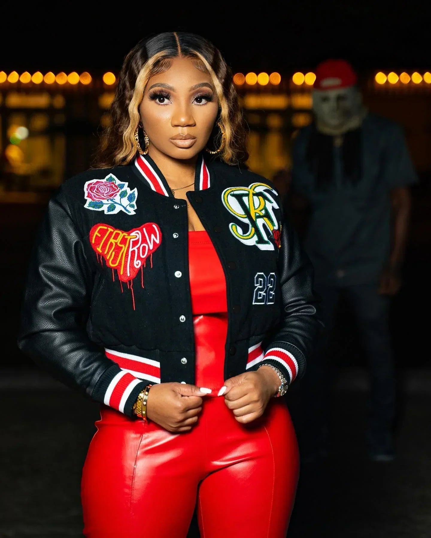 Woman wearing black varsity jacket with patches and red faux leather crop top and pants