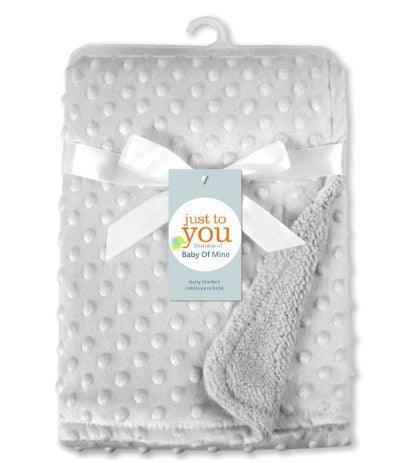 Soft white textured fleece baby blanket with raised dots and smooth satin trim, folded and tied with a ribbon.