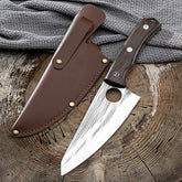 Hand-forged chef knife with rustic wooden handle and leather sheath on wooden surface