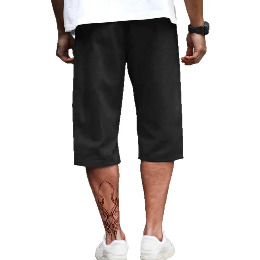 Man wearing loose-fit black knee-length shorts and white sneakers, viewed from behind