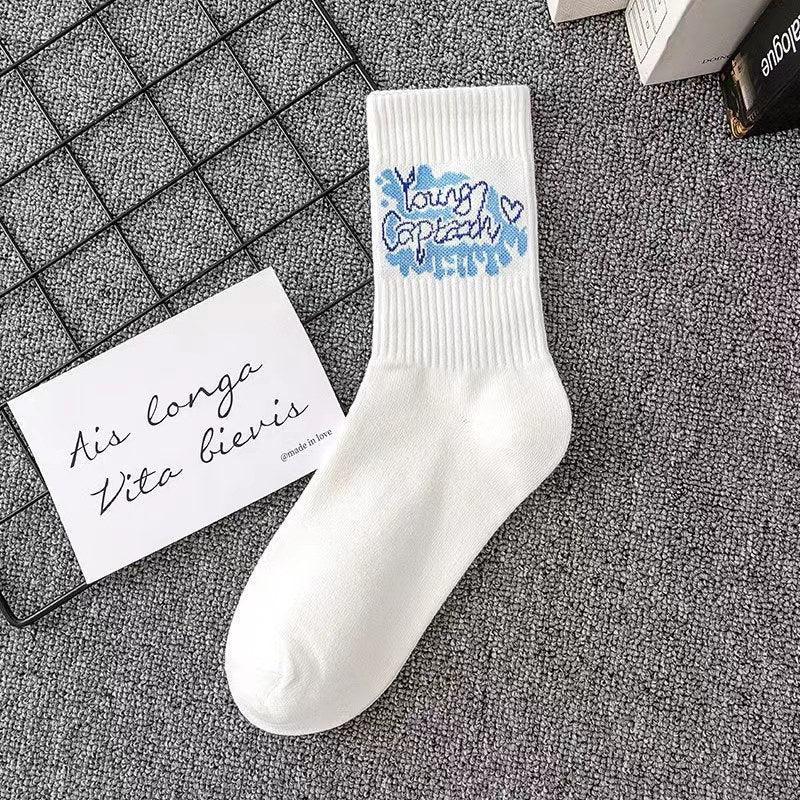 White cotton crew sock with blue graphic embroidery and ribbed top, laid on grey carpet