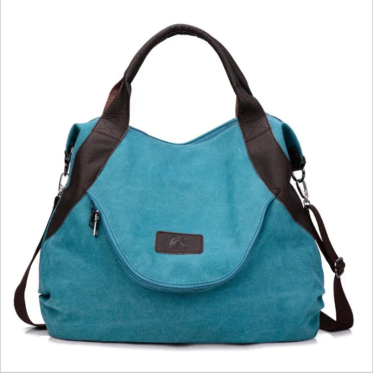Teal canvas tote bag with black faux leather straps and zippered front pocket