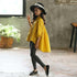 Girl in loose yellow cotton shirt, black skinny jeans, black loafers, and wide-brim hat