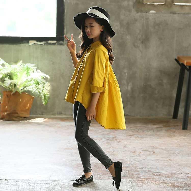 Girl in loose yellow cotton shirt, black skinny jeans, black loafers, and wide-brim hat
