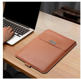 Slim brown faux leather laptop sleeve with magnetic flap on wooden desk next to a laptop.