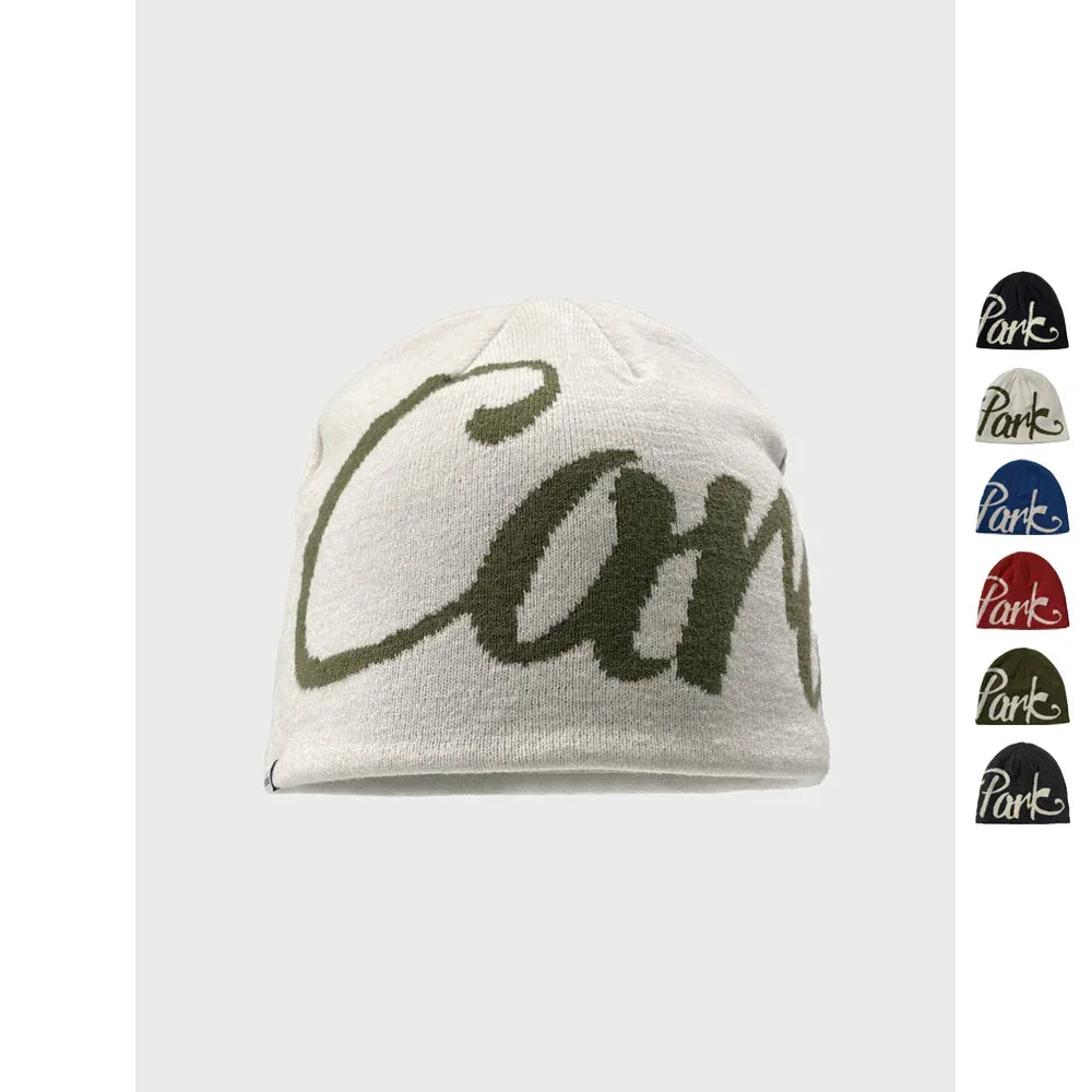 White knit beanie with large green script, cozy streetwear style, available in multiple colors.