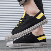 Black canvas low-top sneakers with yellow accent details and distressed rubber soles