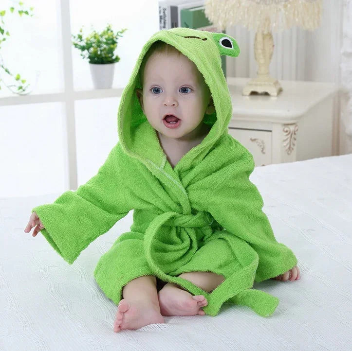 Baby in soft green hooded bathrobe with frog design, sitting on a bed