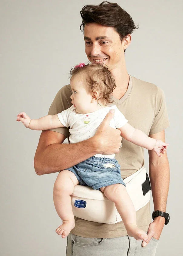 Man in a beige fitted t-shirt holding a baby wearing a white tee and denim shorts on a hip seat