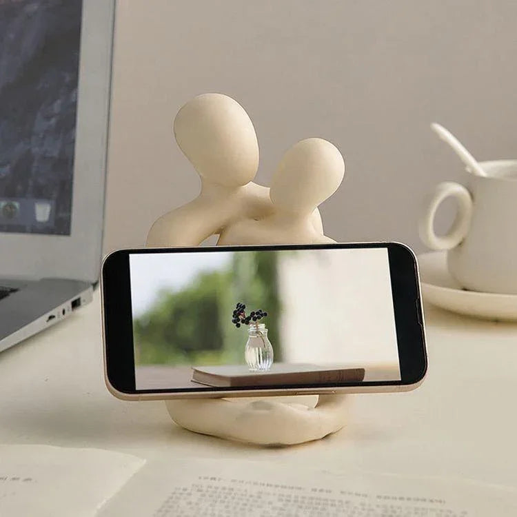 Minimalist beige resin phone holder with abstract human figures on a desk.