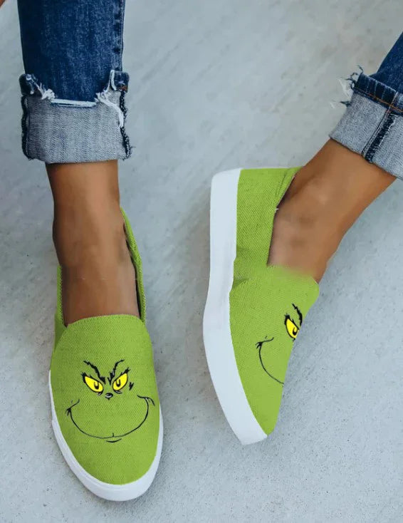 Green canvas slip-on sneakers with cartoon face print, worn with rolled-up jeans.