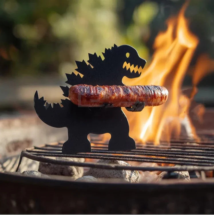 Metal dinosaur-shaped grill tool holding sausage on barbecue with open flame